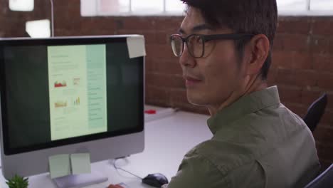 portrait of asian businessman sitting at desk looking to camera smiling