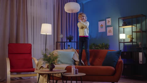 Active-funny-girl-kid-jumping,-dancing,-fooling-on-soft-cozy-sofa-at-home-spend-free-time-alone