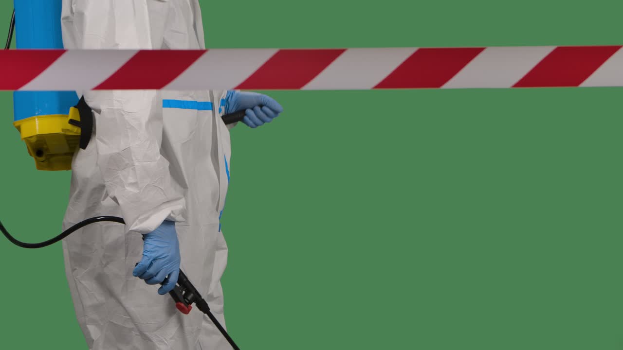 신호 테이프 뒤에서 볼 때, 바이오바이러스 위험에 대항하는 보호복을 입은 의료 직원이 코로나 바이러스에 대한 살균을 위해 화학 물질을 스프레이합니다. 녹색 화면 크로마 키. 느린 모션.
