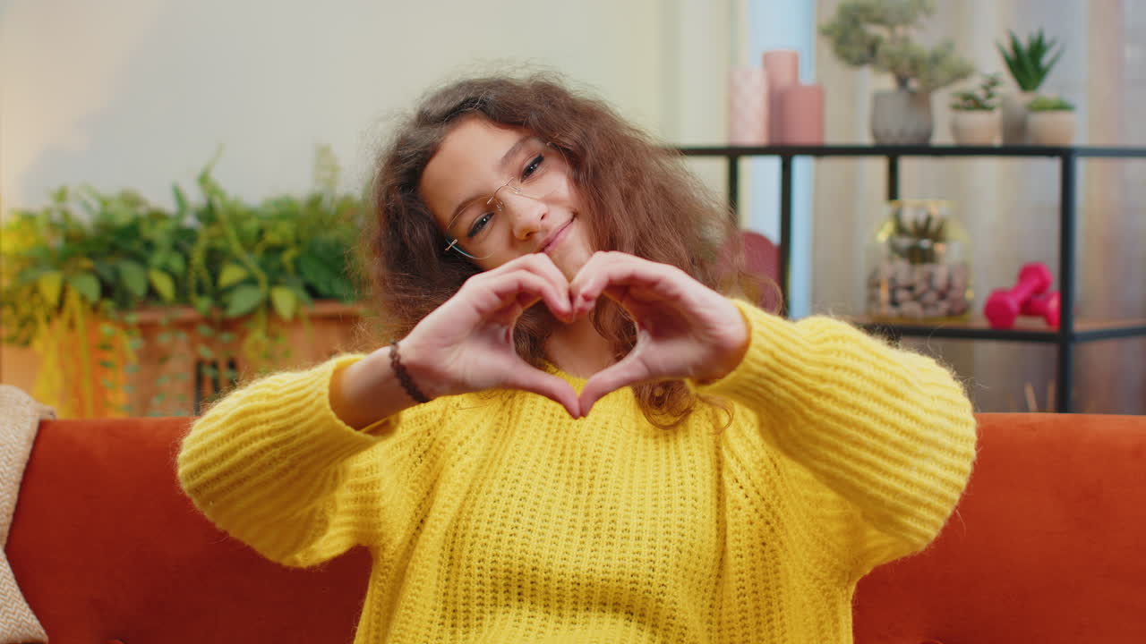 Young child kid girl makes symbol of love showing heart sign to camera express romantic feelings