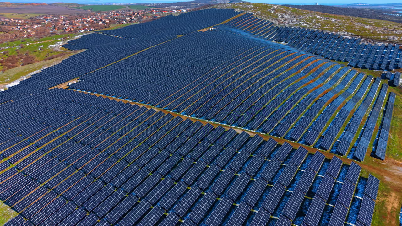 Bredt luftfoto af storstilet solcelleanlæg. Panoramaudsigt over et omfattende solcelleanlæg på en bakke nær en landlig landsby. Blå himmel og koncept for vedvarende energi.
