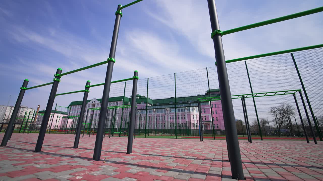 Sport horizontal bars of different height at the modern sport ground. Beautiful pink building with green roof at backdrop. Low angle view.
