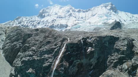 a stunning aerial approach toward the breathtaking glacial cascade of chacraraju, the iconic waterfall feeding turquoise laguna 69 in peru’s cordillera blanca