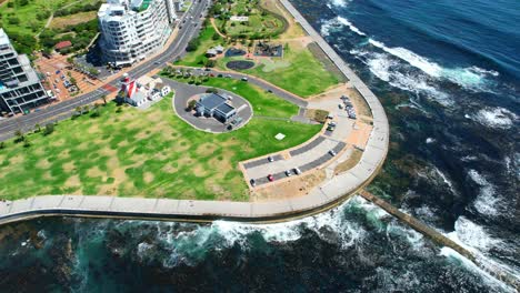 top-down-people-cycling-in-Green-Point-on-a-sunny-summer-day-in-Cape-Town-with-lighthouse,-aerial