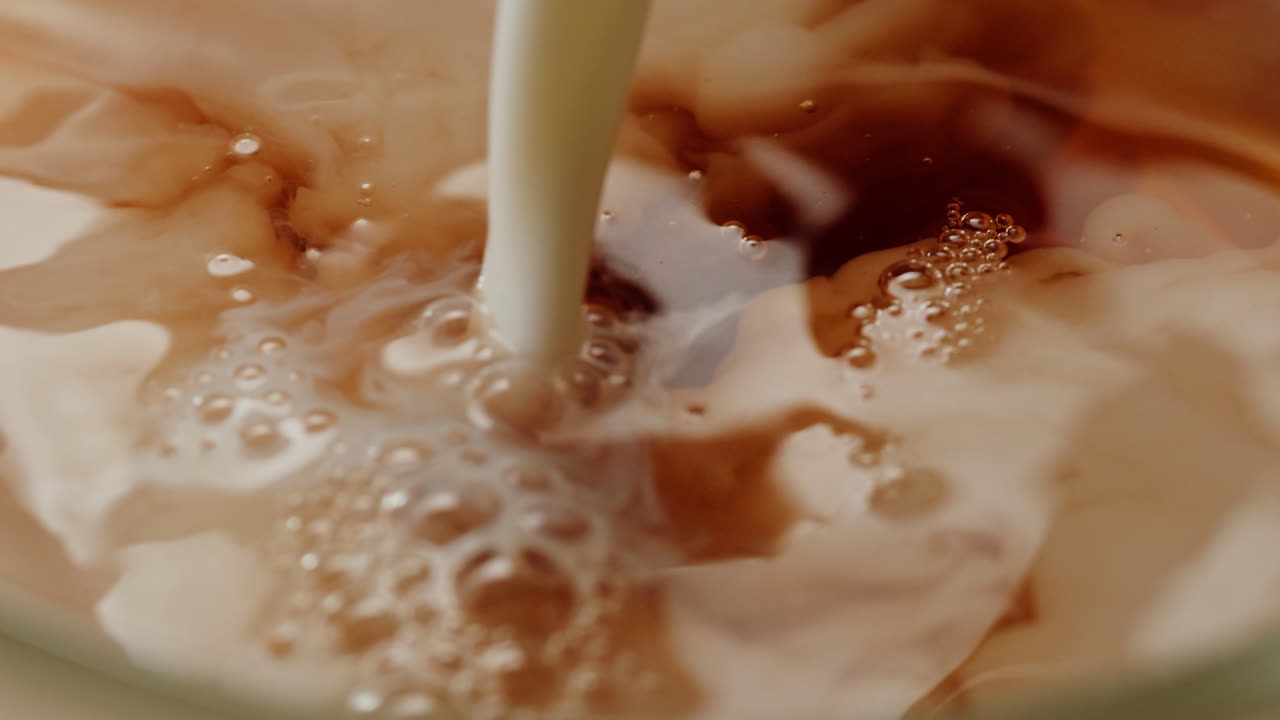 Pouring milk into black tea in glass cup. Drinking hot tea with milk, healthy morning, freshly brewed detox drink. High quality 4k footage