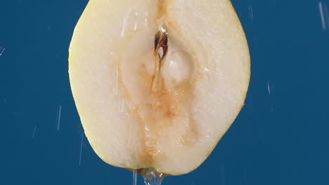 yellow half pear on a blue dark background with drops of water rolling down the pear and flowing splashing with isolated background