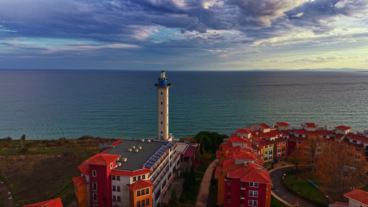 Colorato villaggio costiero con vista sul mare e un faro che si erge alto contro un cielo nuvoloso al crepuscolo vicino alla riva