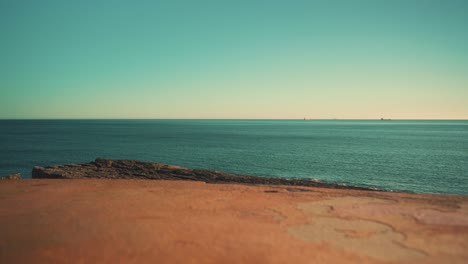 Ocean-shoreline-cliff-with-cargo-boats-away-at-sunset-under-blue-sky-4K