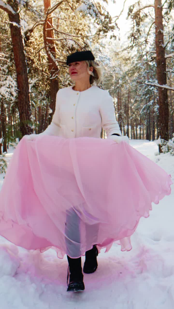 Donna elegante in gonna rosa passeggia giocosamente in una foresta invernale.