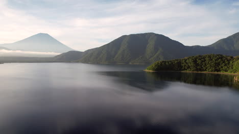 Vista-Aérea-Del-Lago-Motosu-Brilla-Debajo,-Mientras-La-Cámara-Se-Inclina,-Revelando-El-Majestuoso-Monte-Fuji-En-El-Horizonte