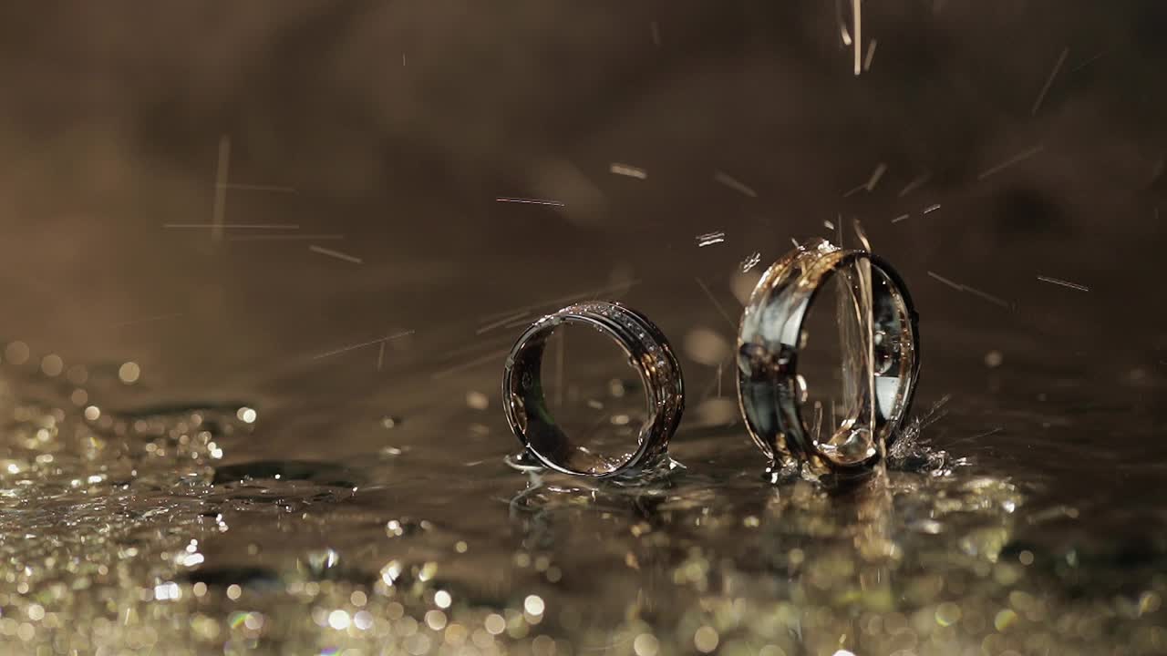 Wedding rings on dark water surface shining with light. Water drops. Close up