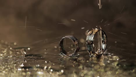 Wedding-rings-on-dark-water-surface-shining-with-light.-Water-drops.-Close-up