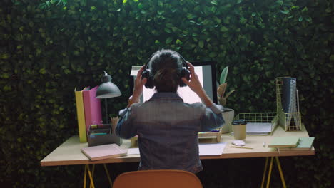 joven mujer de negocios que trabaja hasta tarde usando la computadora navegando en línea planeando una estrategia creativa de inicio escuchando música usando auriculares en la oficina por la noche