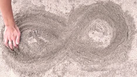 a contemplative image of a woman hand creating an infinity symbol in the sand. inner peace and relaxation concept