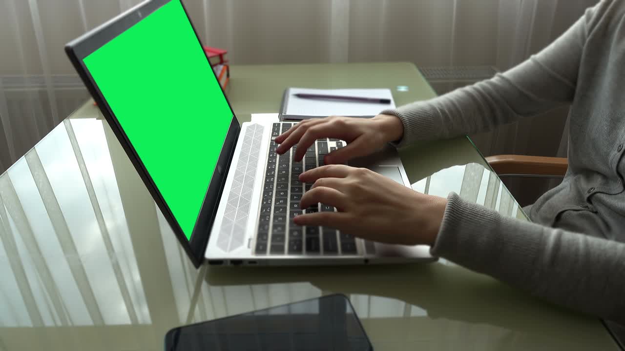 The girl working at home office hands on keyboard. The screen is a green background.