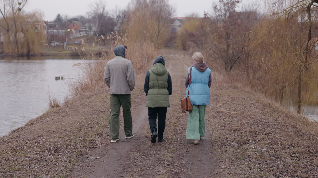 три человека идут по тропе у озера осенью и зимой.