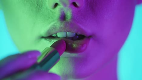acercamiento extremo de los labios de una hermosa mujer llena mientras se aplica lápiz labial rojo y se prepara para la noche o la cita con contraste púrpura verde en su cara