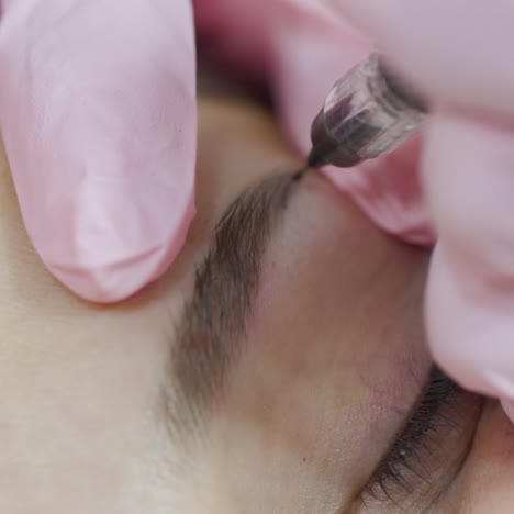 cosmetologist in gloves is correcting the shape of a woman's eyebrows with a professional needle. the procedure of permanent eyebrow makeup.