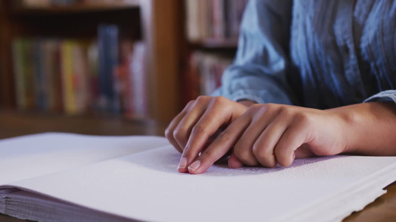 estudiante asiática sentada y tocando una página de un libro en braille en la biblioteca