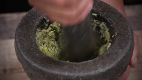 golpeando ingredientes frescos con mortero de piedra y mortero, cocinando con pasta fresca de cerca