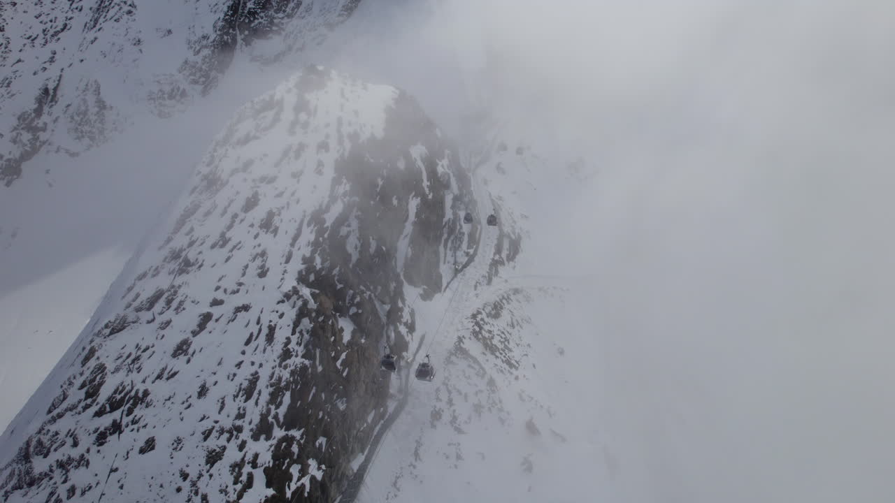 Moving Gondolas at ski lift through dense fog in snowy mountains of Austria - Aerial top down