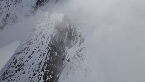 Góndolas-En-Movimiento-En-El-Remonte-A-Través-De-Una-Densa-Niebla-En-Las-Montañas-Nevadas-De-Austria---Antena-Arriba-Hacia-Abajo