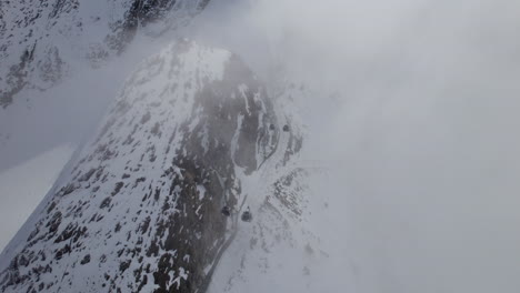 moving gondolas at ski lift through dense fog in snowy mountains of austria - aerial top down