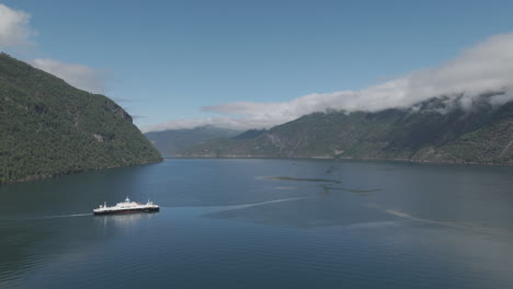 drone shot of a car ferry crossing the fjord in norway on a sunny day with clear water and reflections and mountains in the background with clouds between them log