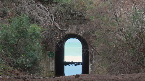 cyclist rides past tunnel leading to wild sea