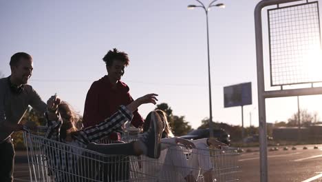 vista lateral de unos jóvenes amigos divirtiéndose al aire libre en carritos de compras