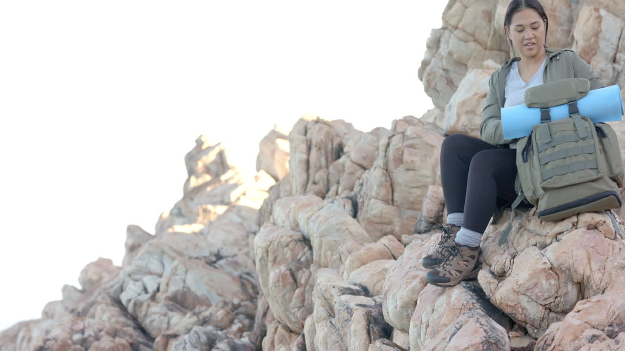 Hiking in mountains, woman sitting on rocks and unpacking backpack with gear, copy space