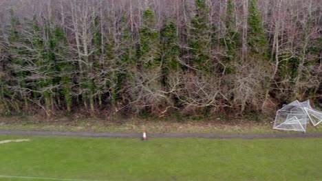 aerial overview tracking left of damaged woodland with uprooted trees and scattered branches along path with broken football goals, barna woods, galway ireland