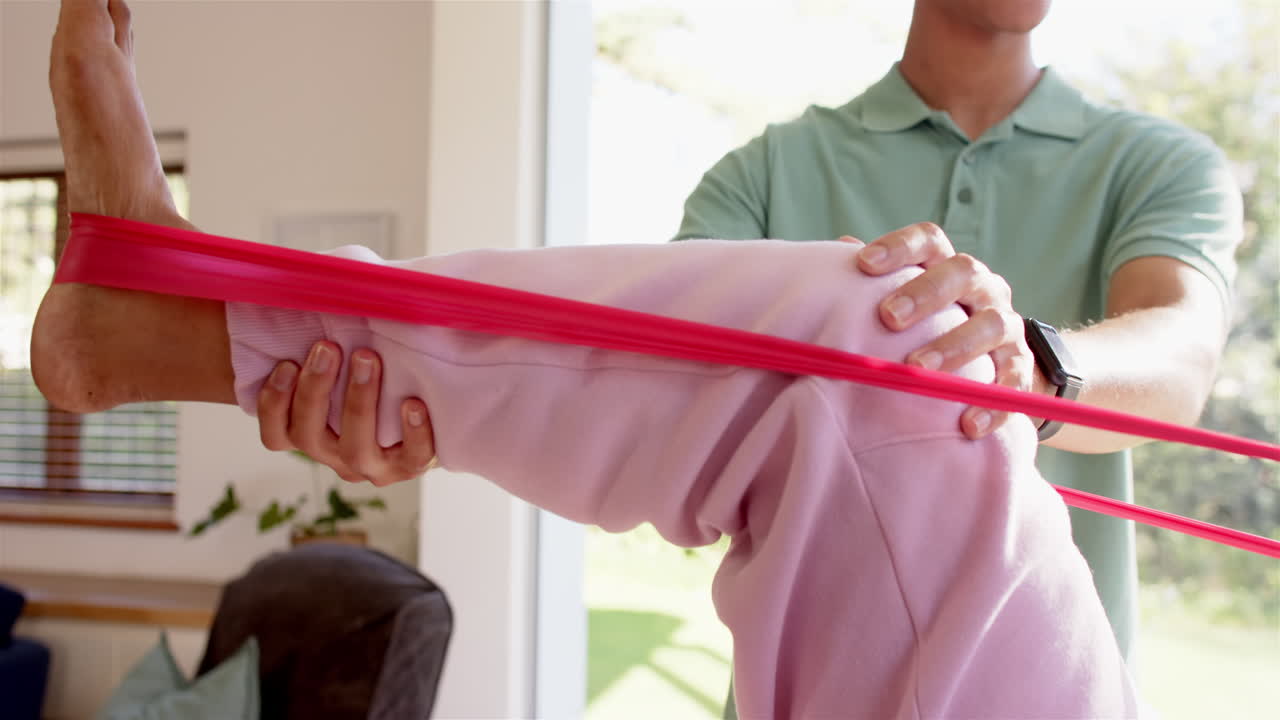 Physiotherapist assisting senior woman with leg exercise using resistance band