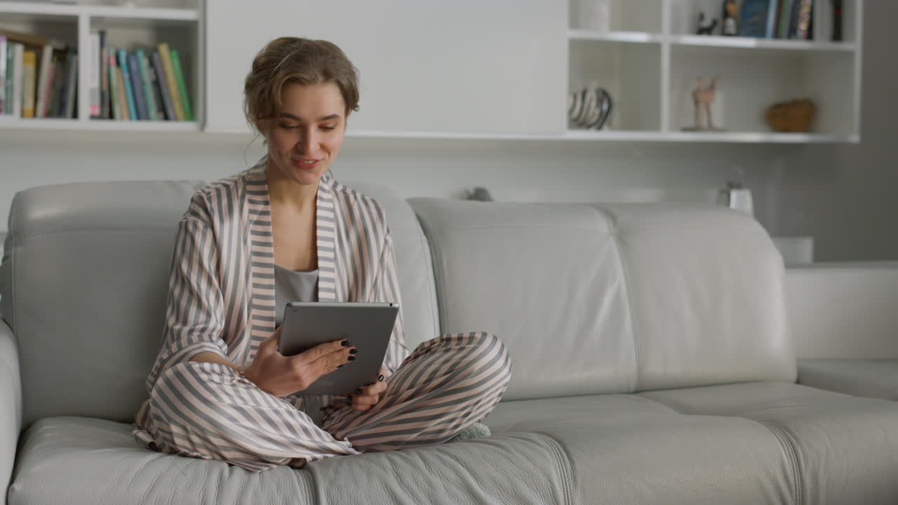 Student having online video conversation in living room. Smiling girl using pad