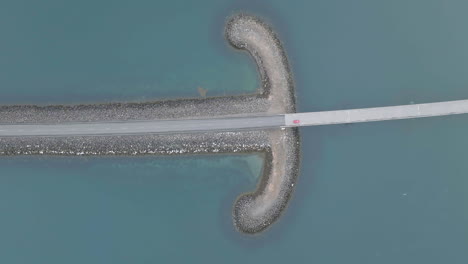 birds eye aerial view of car moving on road between breakwaters on glacial lake in landscape of iceland