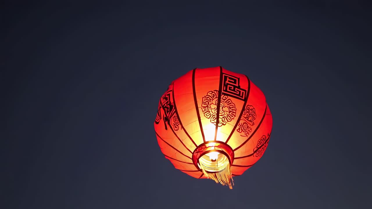 Low-angle video shot of a glowing red lantern against a dark sky, highlighting its intricate