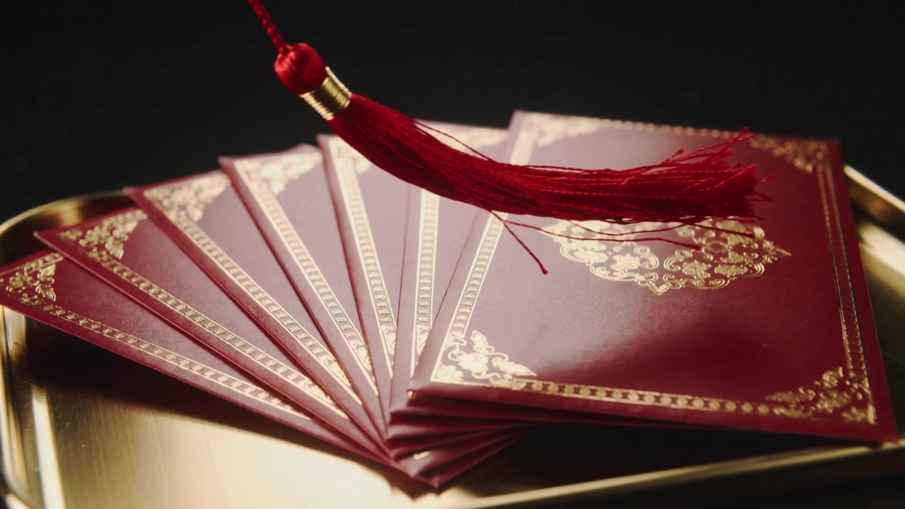 Sweeping suspended red tassel brushing fanned red envelopes on gold tray, being pulled off-frame