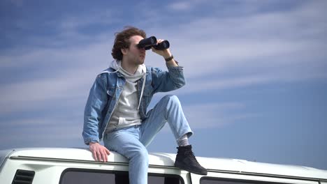 young boy looks around with a pair of binoculars on the roof of a caravan.