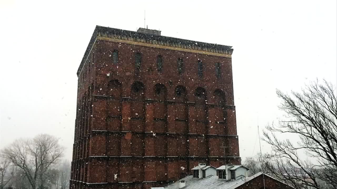 Fiocchi di neve al rallentatore durante una nevicata molto abbondante, con un alto edificio in mattoni rossi sullo sfondo.