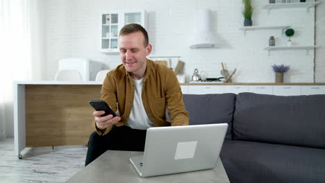 man working at home. young freelancer sitting in front of a laptop and using mobile phone in the kitchen. distance education. coronavirus. covid-19.