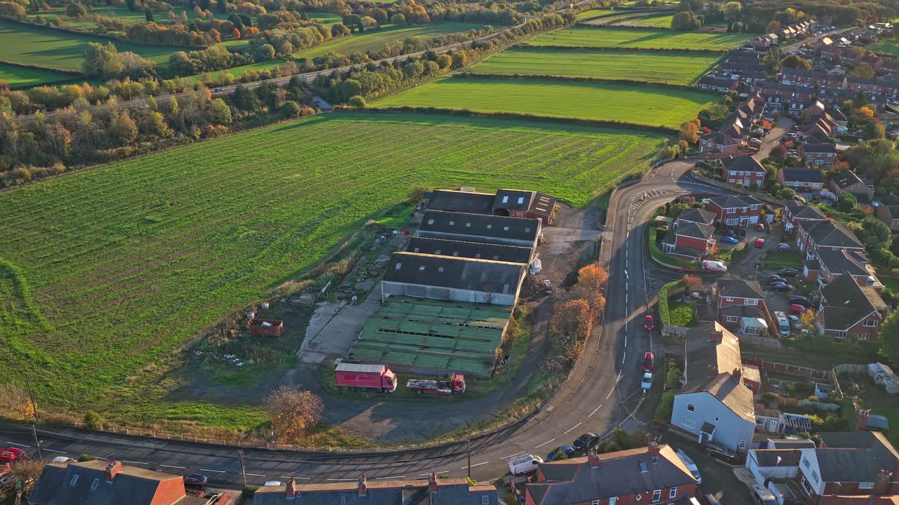 Farming facility in Hemingfield, Barnsley, showing corrugated roof sheds for livestock, cultivated fields, and nearby brick housing under late afternoon light, drone push in