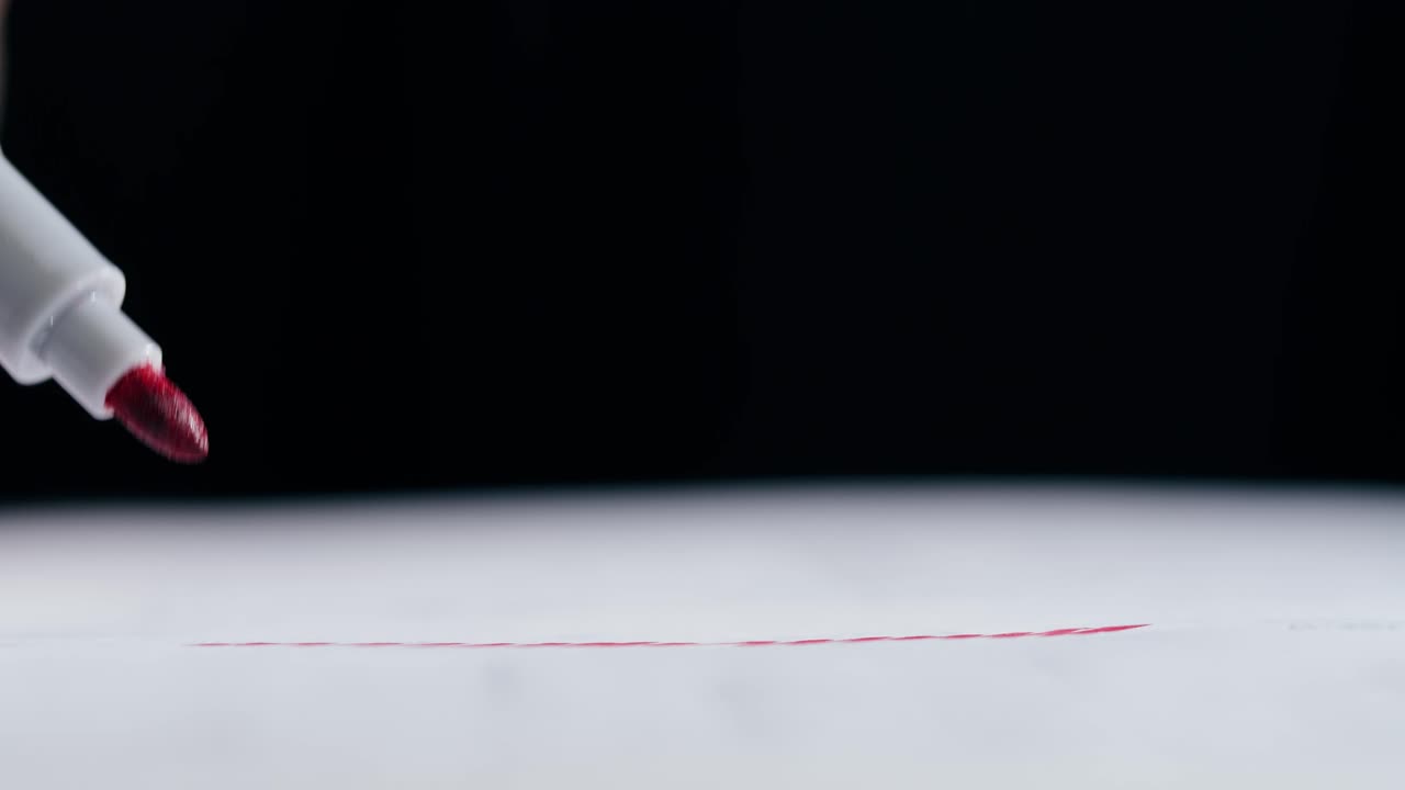 Close-up of a marker drawing a red line on white paper