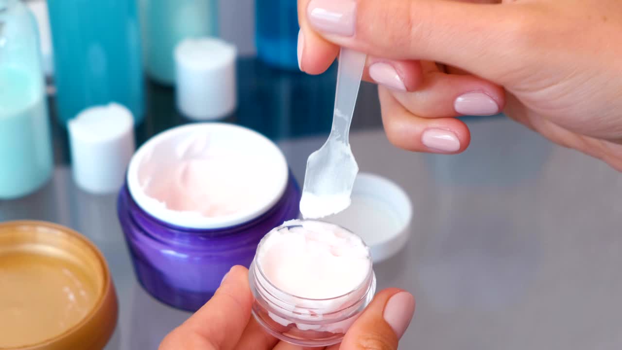 las manos de las mujeres ponen la crema de un frasco grande en uno pequeño con una espátula. conjunto de cosméticos de carretera. frascos de primer plano. vista superior.