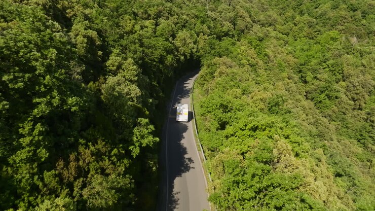 Tehlikeli, yüksek rakımlı bir orman yolunda ilerleyen bir karavana eşlik eden drone