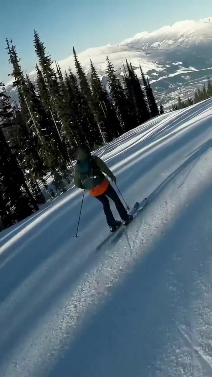 Video verticale: Snowboarder con giacca rossa, seguito dalla telecamera, traccia una linea sulla pista, evitando gli sciatori.