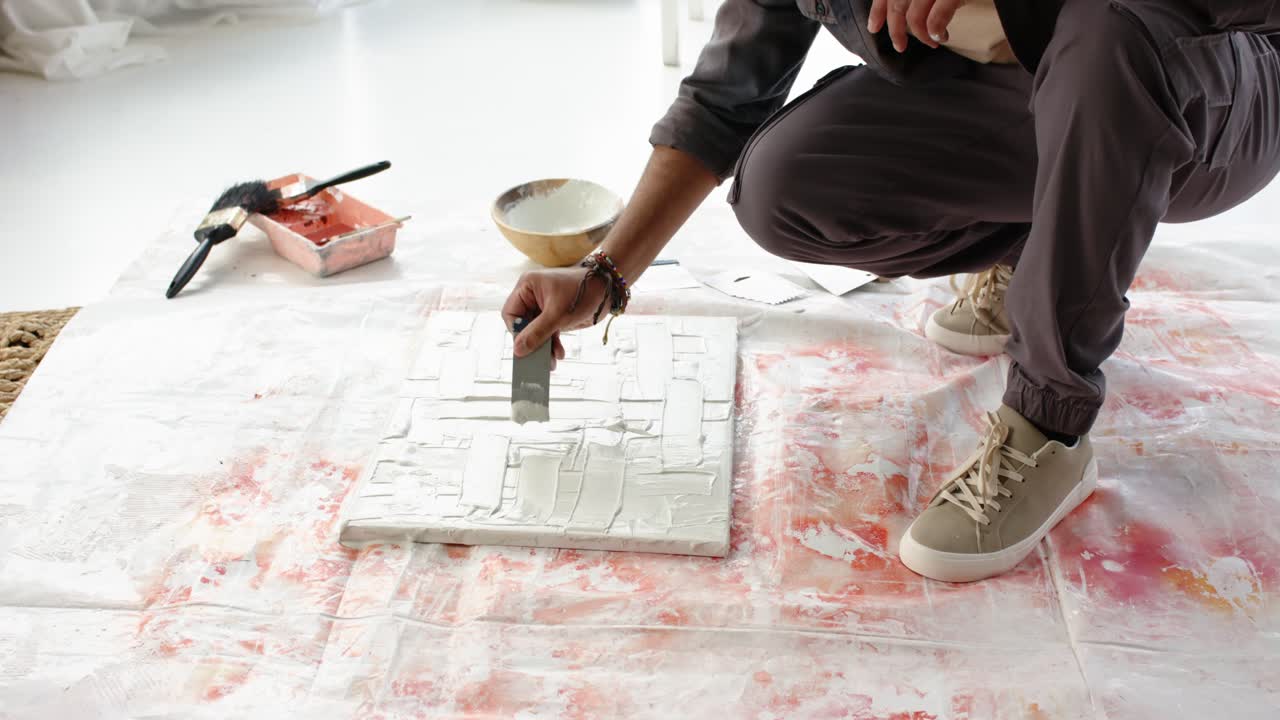 I første sekund skraber en latinamerikansk mandlig kunstner medium og udglatter lærredet i studiet for at dække det