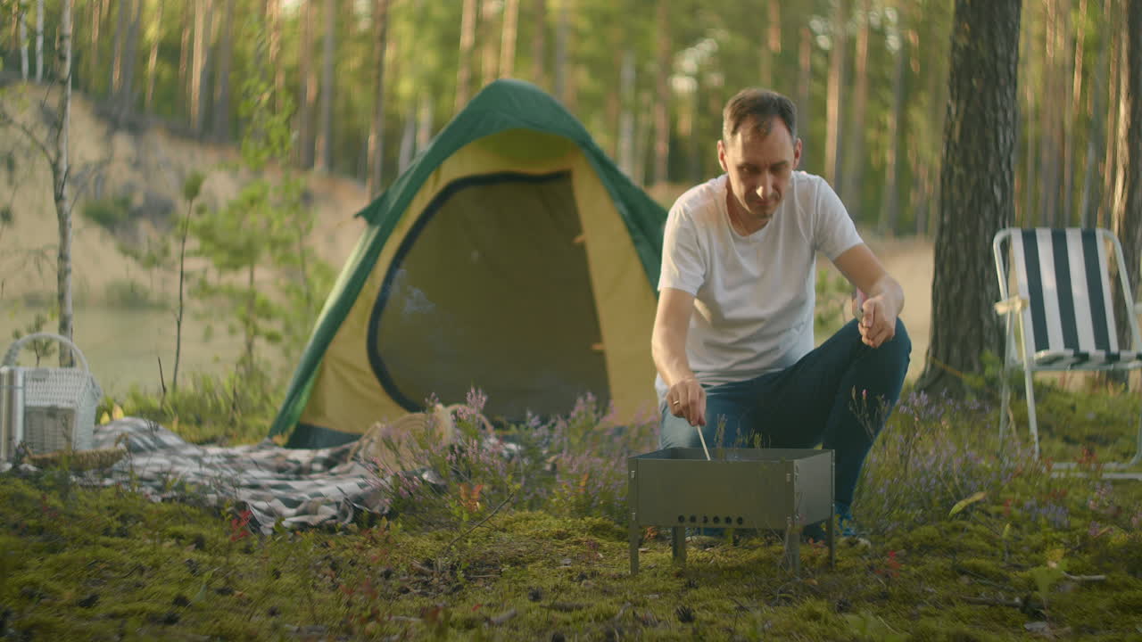 el turista vive solo en el campamento del bosque encendiendo carbón en la parrilla para cocinar la cena. viaje al bosque en vacaciones de verano.