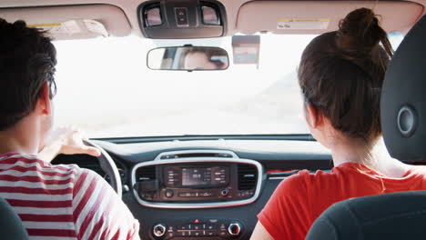 Young-white-couple-driving-on-highway,-pointing,-back-view