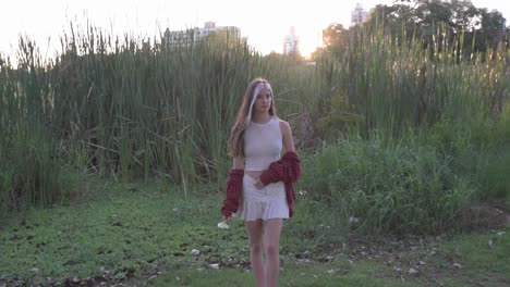 beautiful young woman smelling flower while walking in sunlit nature at sunset