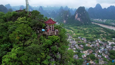 aerial orbit shot around a couple of hikers in a small pagoda in laozhai hill revealing whole xingping and its mountainous environment